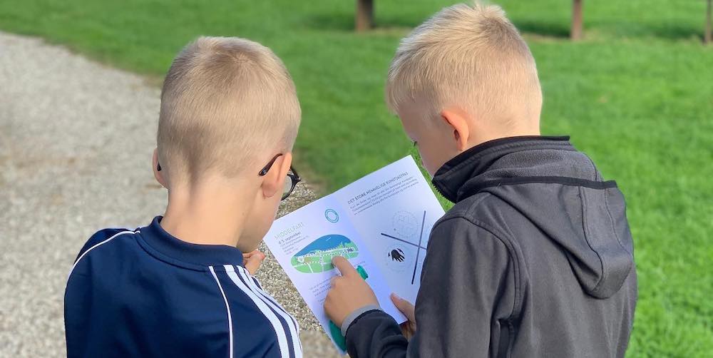To drenge undersøger et kort i en folder ude på en sti.